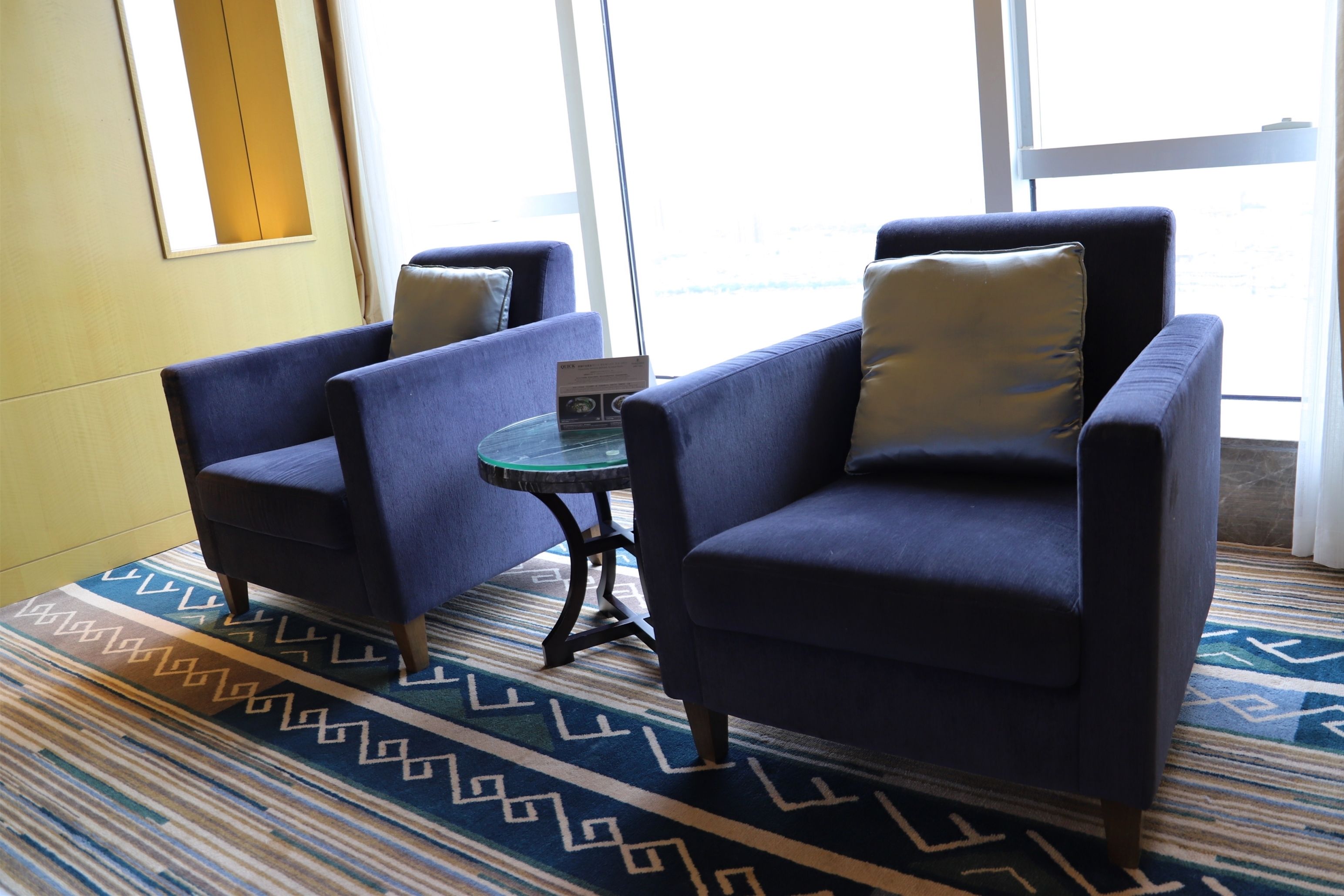 A room with two blue armchairs, a small glass table, and a patterned rug.