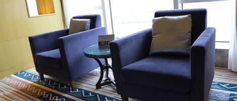 A room with two blue armchairs, a small glass table, and a patterned rug.