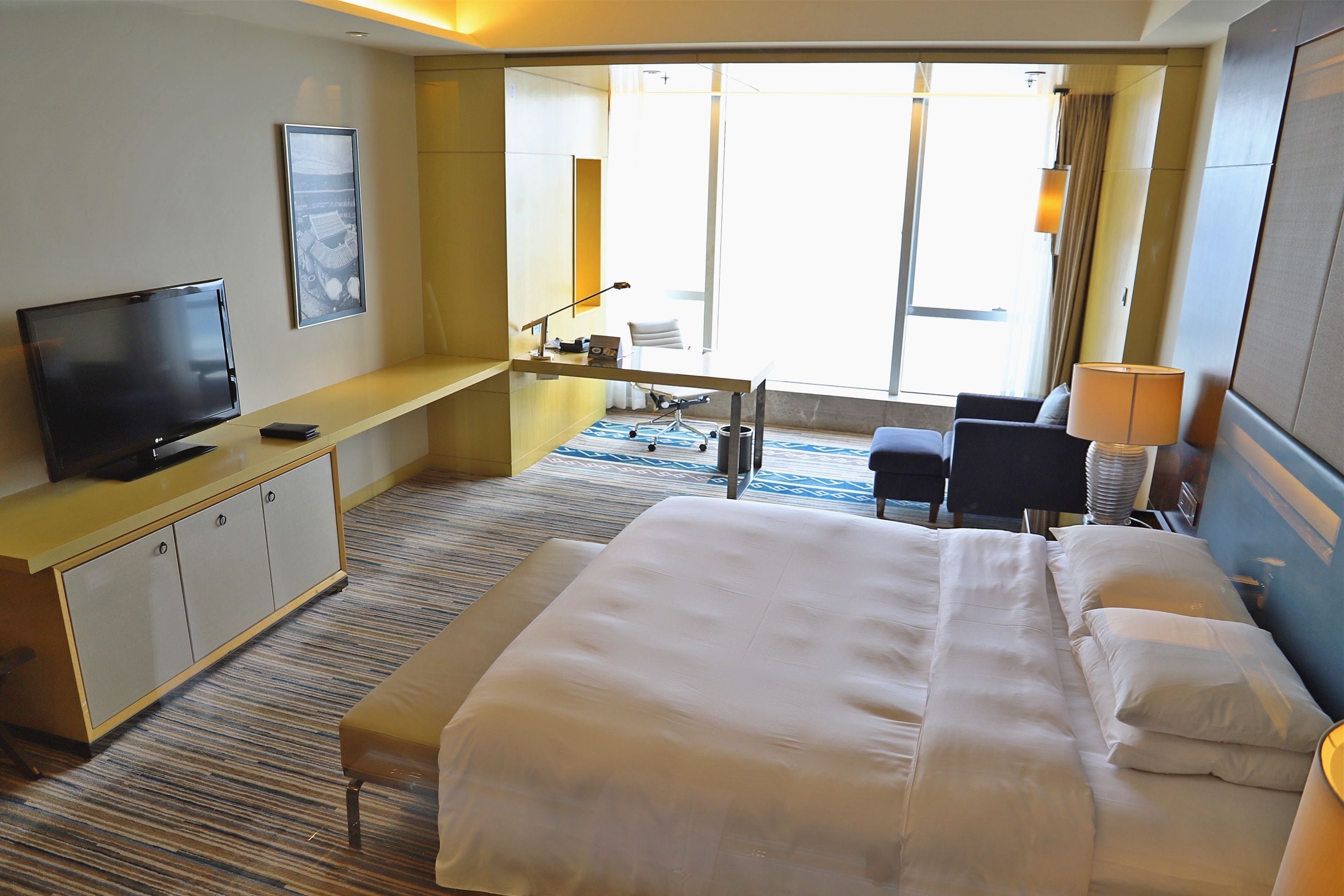Une chambre d’hôtel avec un grand lit, un bureau avec un ordinateur, une télévision et une vue sur l’extérieur.