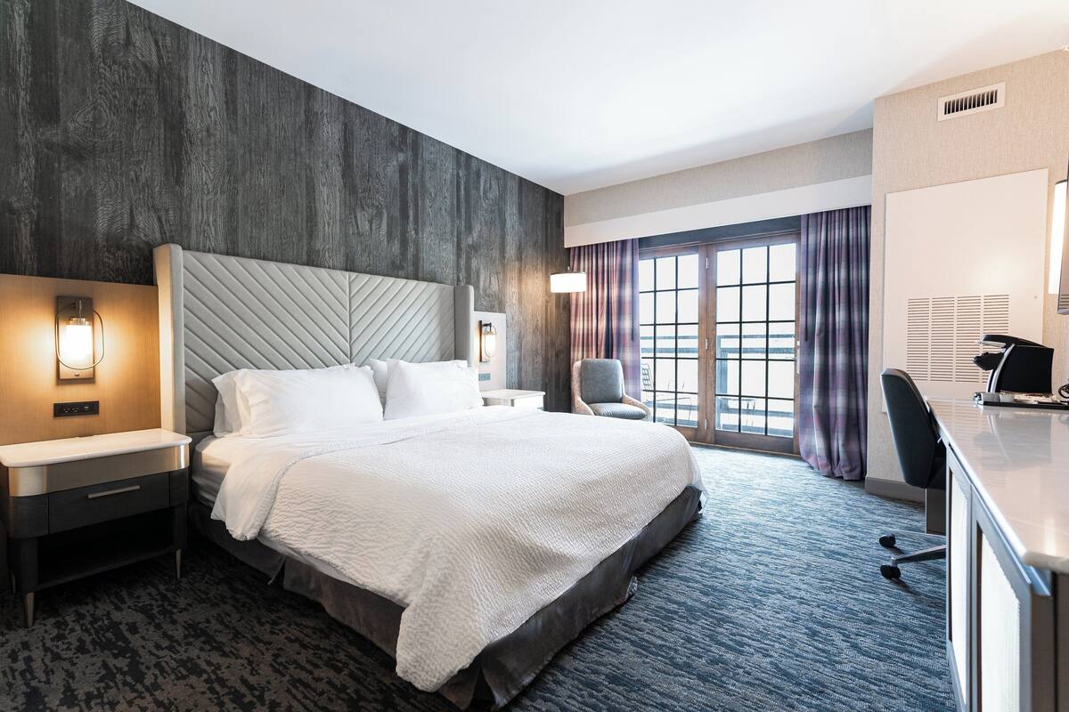 A modern hotel room with a large bed, a desk, and a chair.