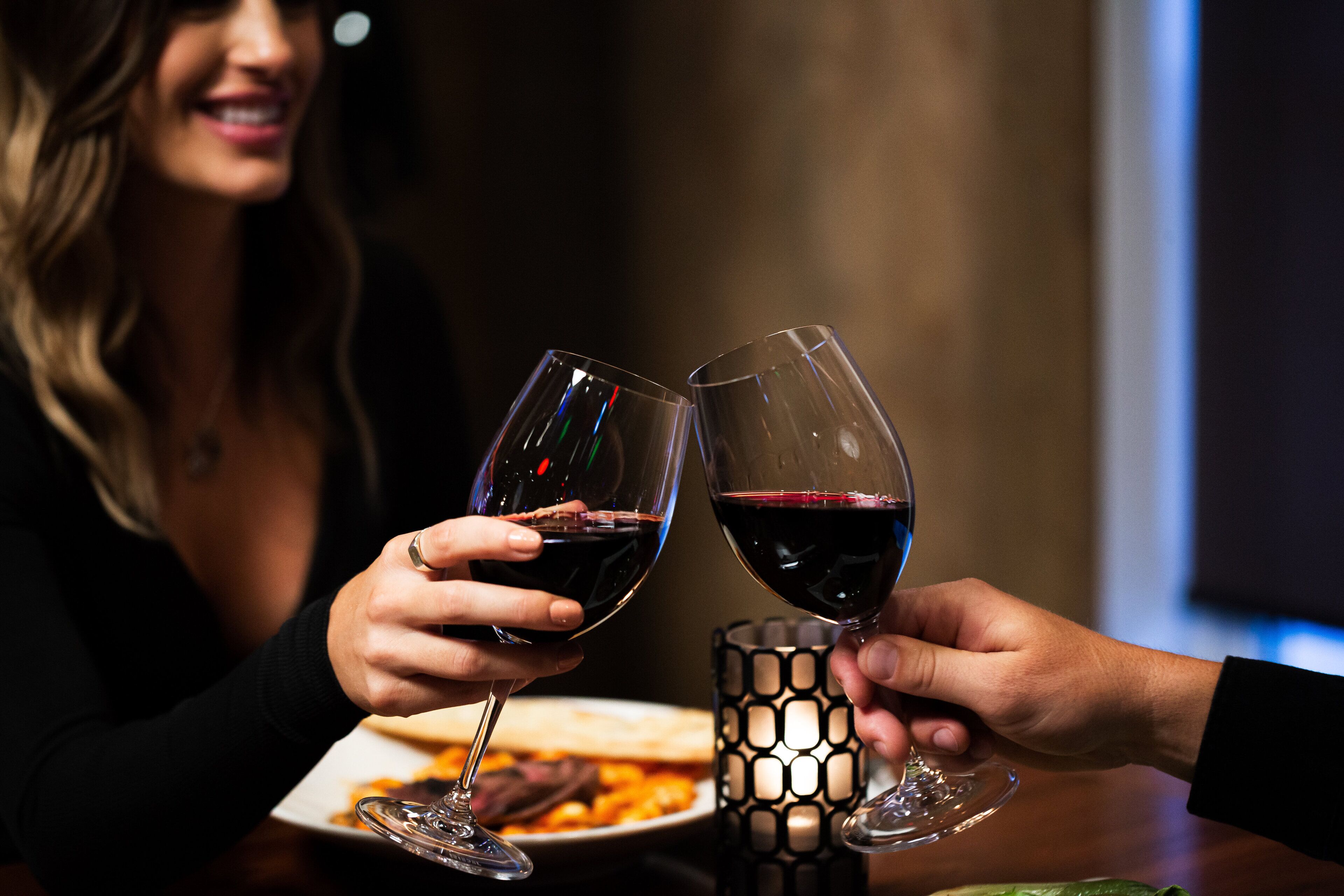 Dos personas brindando con copas de vino en una mesa con un candelabro y un plato de comida.