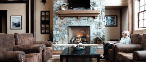 A cozy living room with leather sofas, a stone fireplace, a flat-screen TV, and a coffee table.