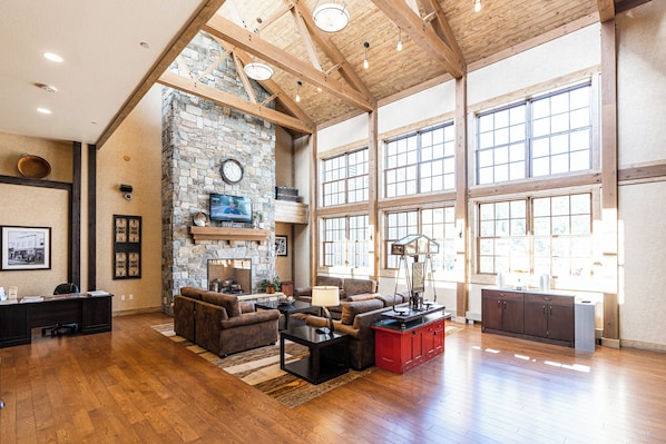 A spacious living area with a stone fireplace, wooden beams, and large windows.