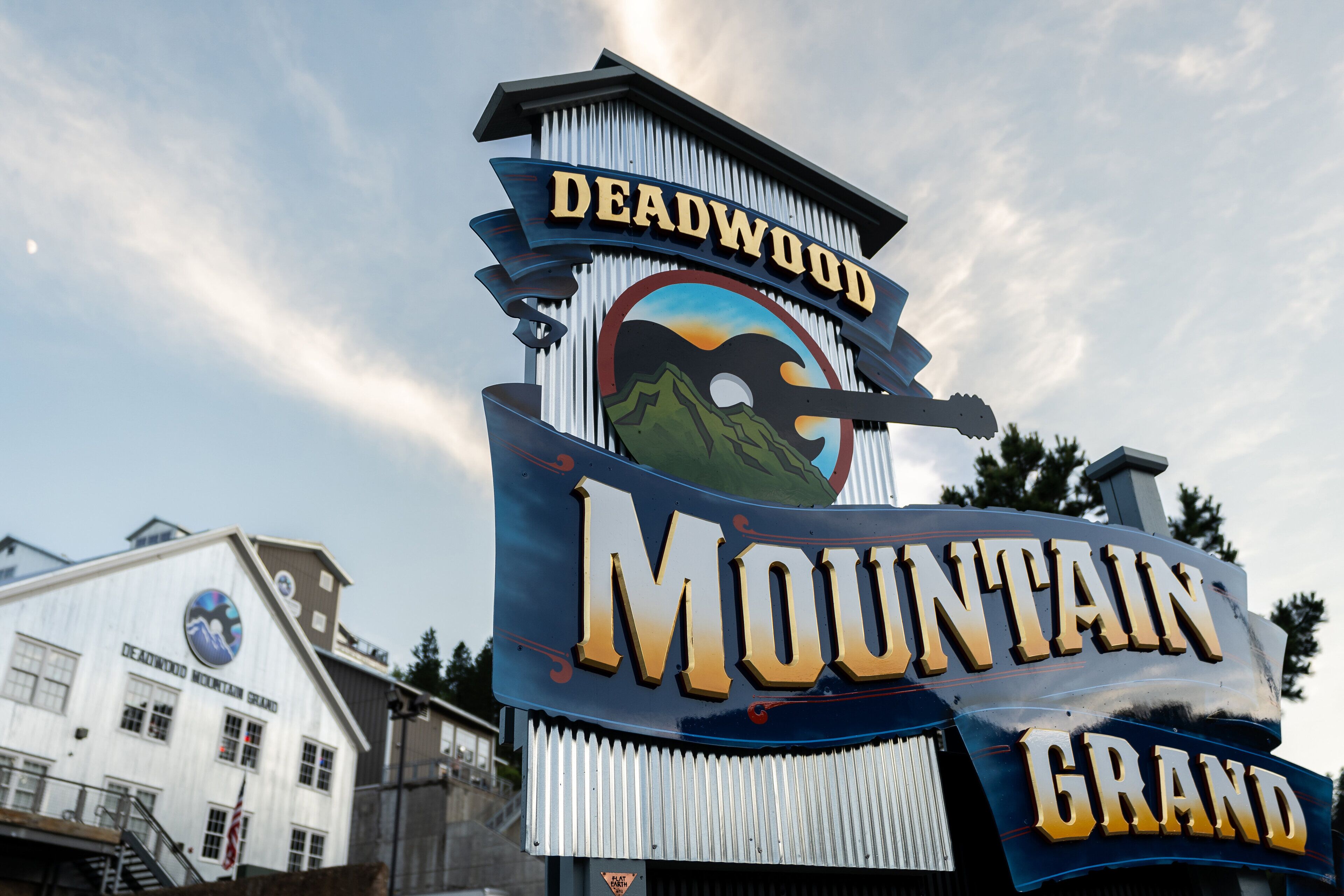 A sign with 'Deadwood Mountain Grand' written on it, with a mountain graphic and a cowboy hat.