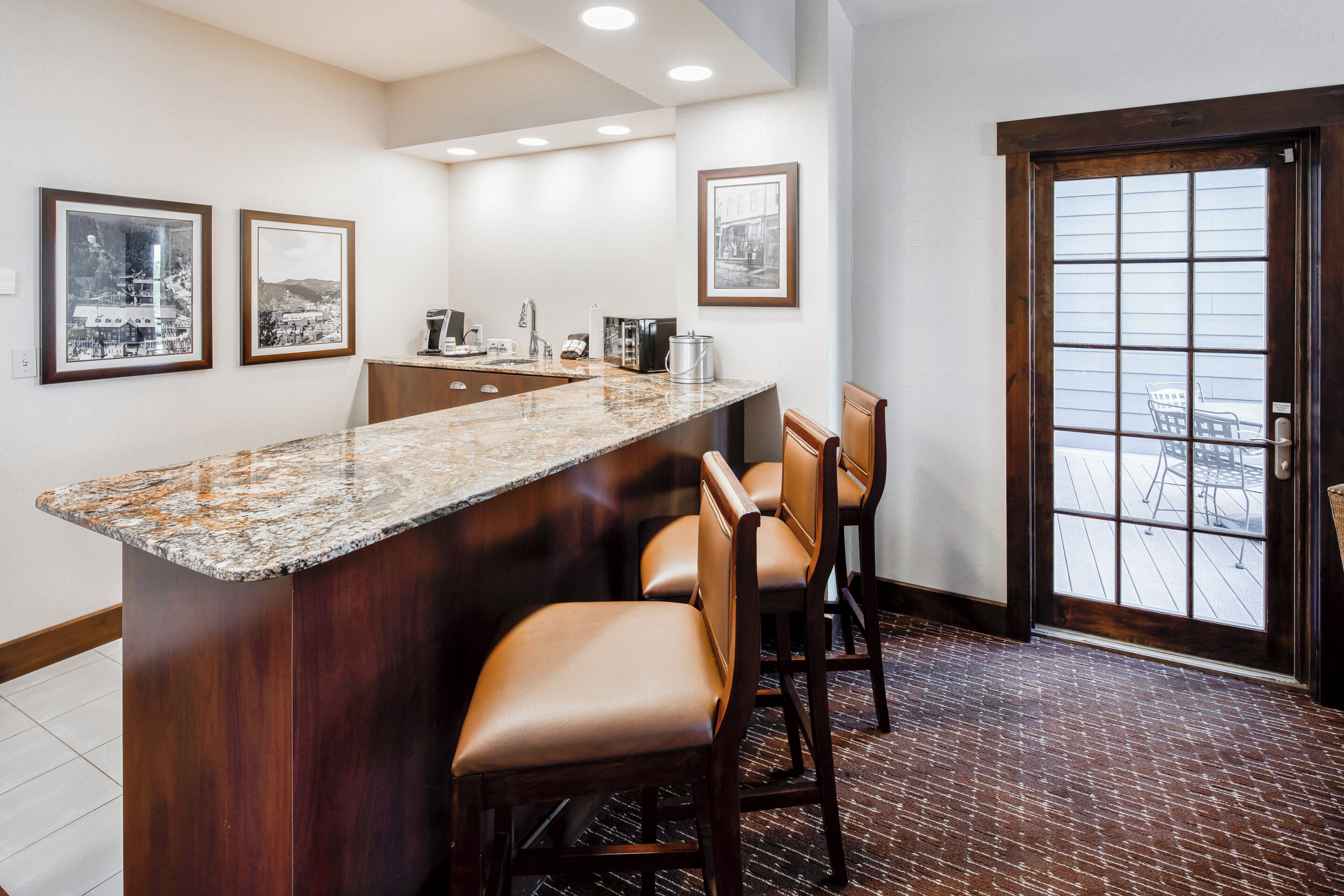 A bar area with a granite countertop, bar stools, and framed pictures on the wall.