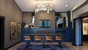 Un espace repas moderne doté d’une grande table de bar, de plusieurs chaises, d’un téléviseur et d’un lustre suspendu.