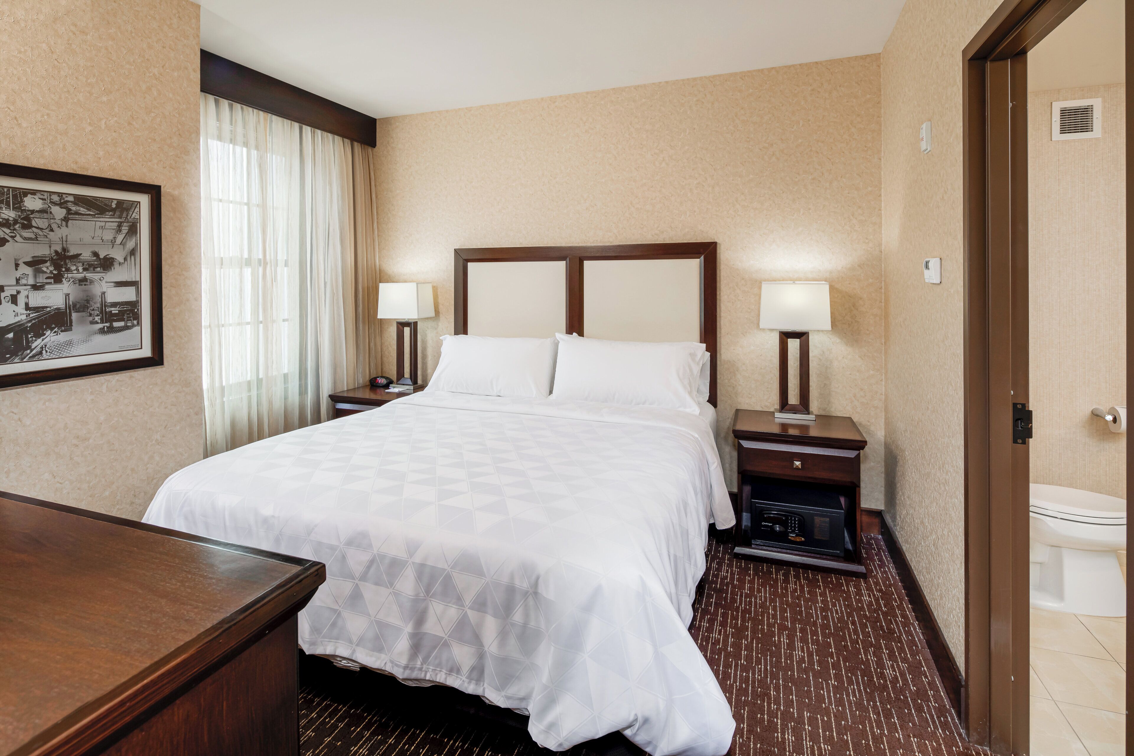 A hotel room with a large bed, two bedside tables with lamps, a framed picture on the wall, and a door to the bathroom.