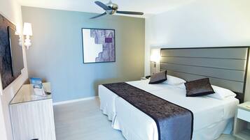 A hotel room with a bed, a nightstand, a lamp, a ceiling fan, and a wall-mounted artwork.