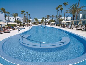 Une grande piscine à eau claire, à bords incurvés, entourée de palmiers et de chaises longues.