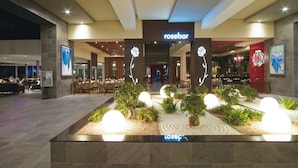 Un bar de rosas con una decoración moderna, una zona de estar con mesas y sillas, y un jardín ajardinado con plantas e iluminación esférica.
