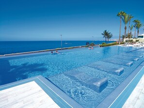A large infinity pool with clear blue water, a tiled deck, and a view of the ocean. - Hotel Riu Palace Meloneras (San Bartolomé de Tirajana)