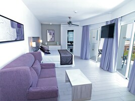 Una habitación de hotel moderna con cama, sofá, televisor y balcón con cortinas.
