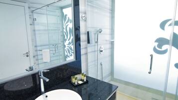 Un baño moderno con un espejo grande, un lavamanos blanco, cabina de ducha con mampara de vidrio y encimera de mármol.