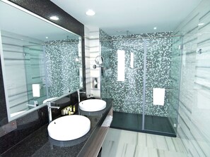 Une salle de bain moderne avec deux vasques, une douche à l’italienne en verre et un grand miroir.