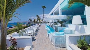 Un patio de resort con mobiliario exterior, palmeras y vista al océano.