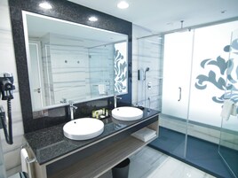 Un baño moderno con dos lavabos, un espejo grande y cabina de ducha con mampara de vidrio.