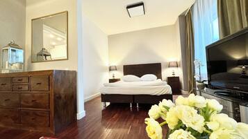 Een hotelkamer met een bed, nachtlampjes, een televisie, een dressoir, een spiegel en een bloemenvaas.