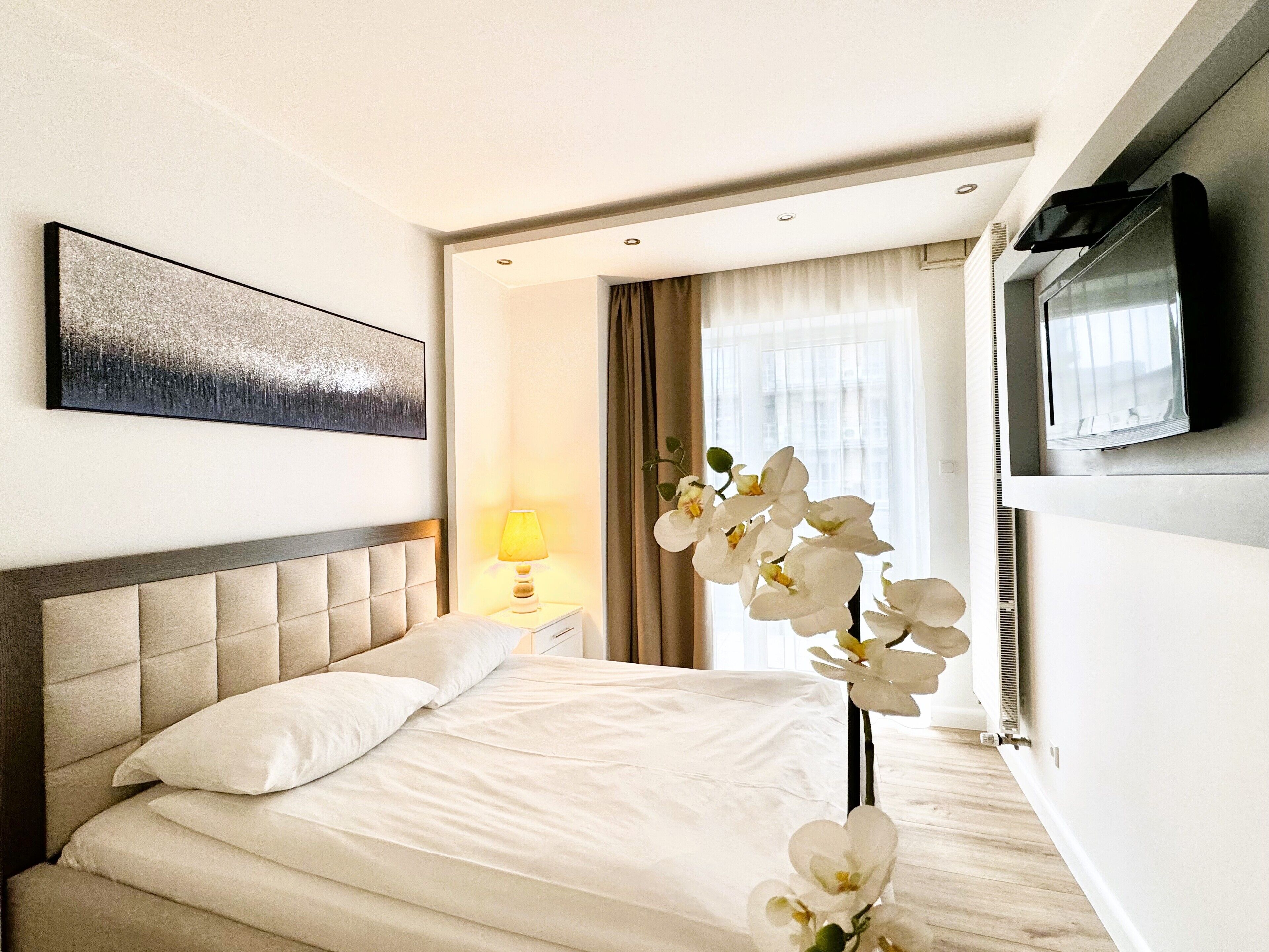 A hotel room with a bed, a nightstand, a lamp, a TV, and a window with curtains.