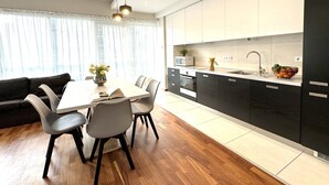 A modern kitchen with dark cabinets, a white countertop, and a dining area with a table and chairs. - Platinum Towers Country 2 Country (Warsaw)