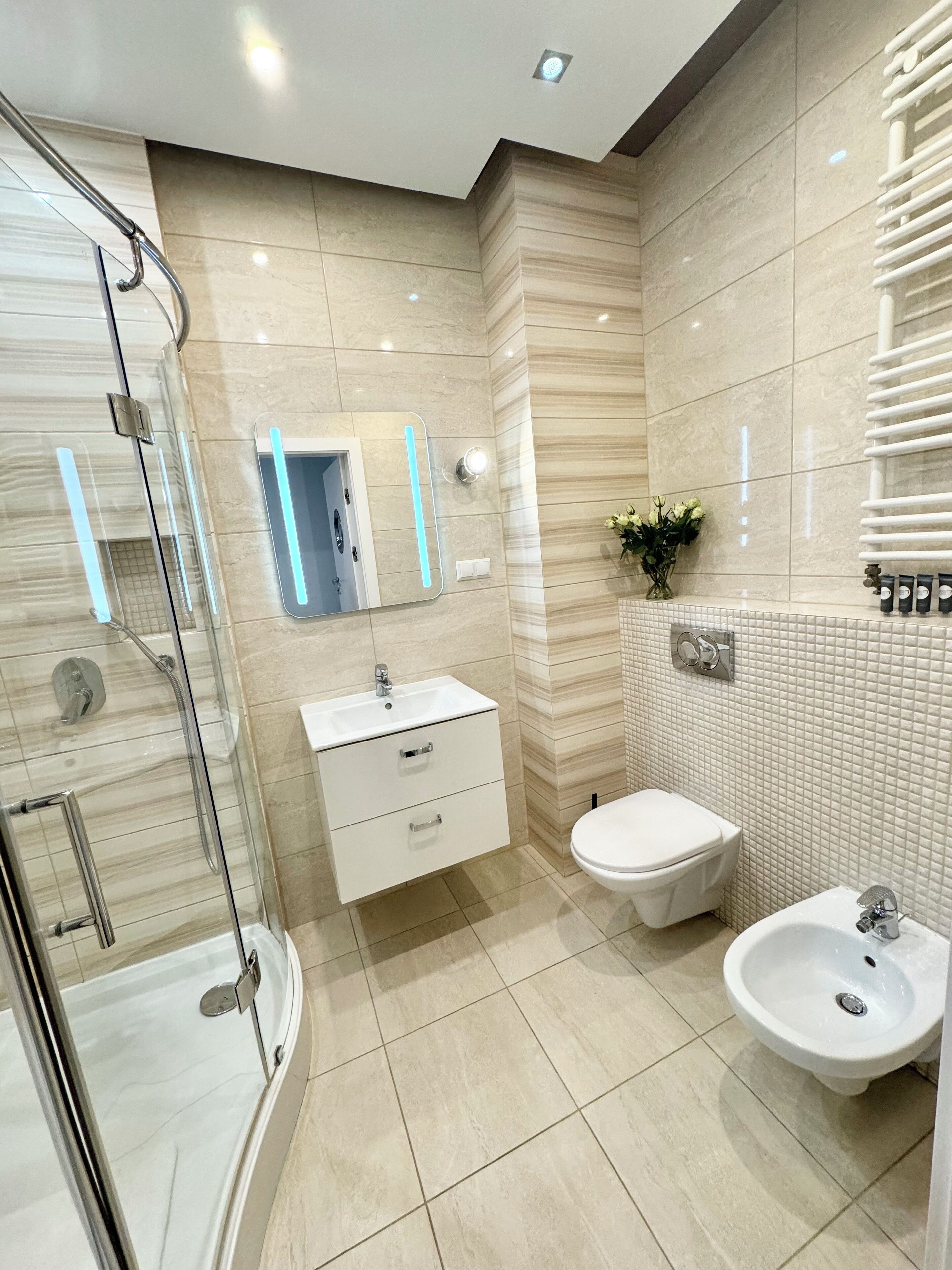 Une salle de bain moderne avec une douche à l’italienne en verre, un lavabo blanc et un bidet.
