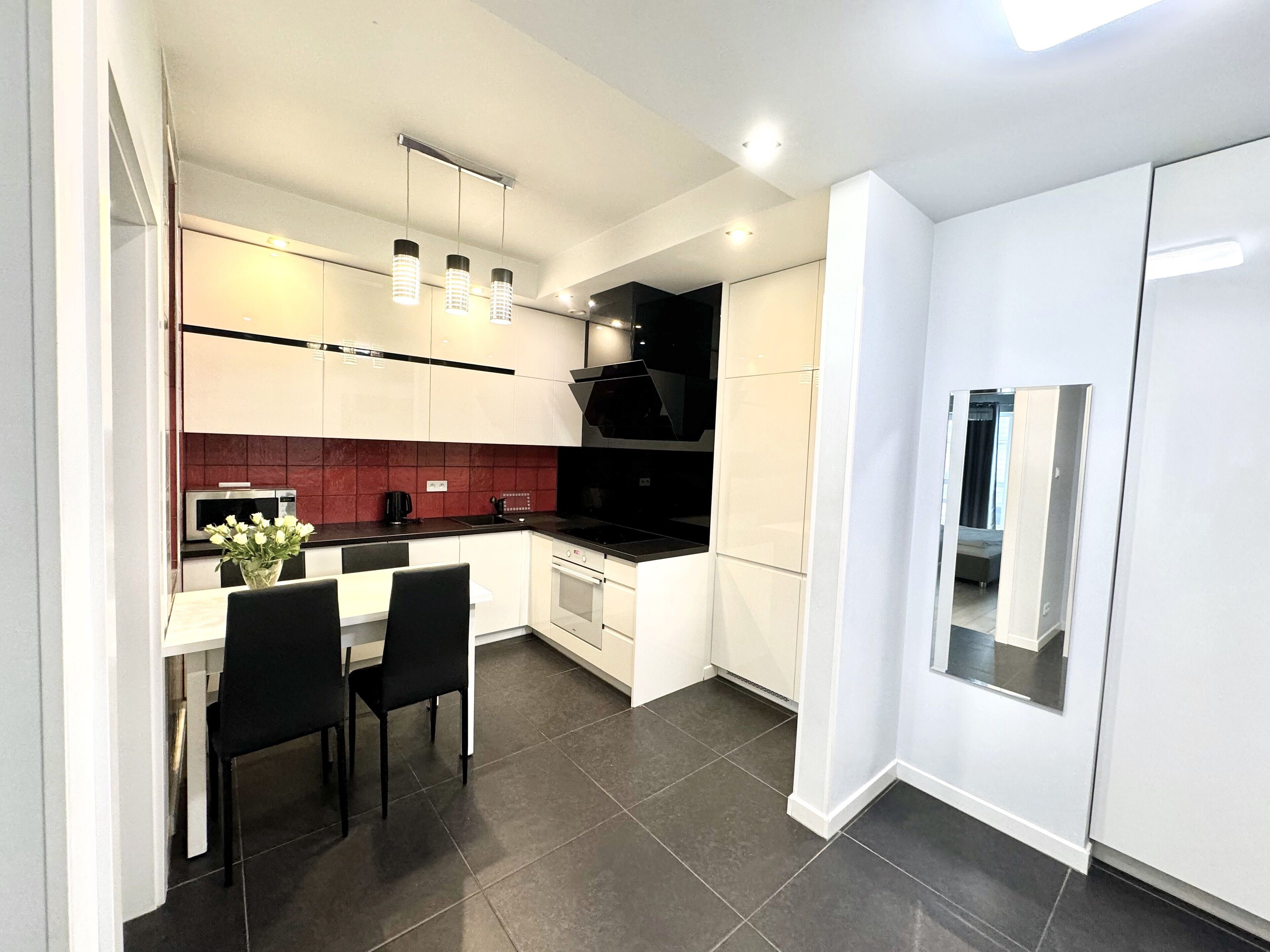 A modern kitchen with white cabinets, a black countertop, and a dining area with two chairs.