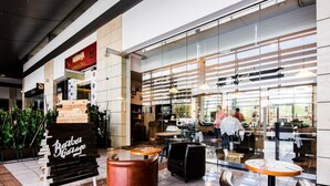 A modern cafe with a glass facade, outdoor seating, and a visible kitchen area. - Platinum Towers Country 2 Country (Warsaw)