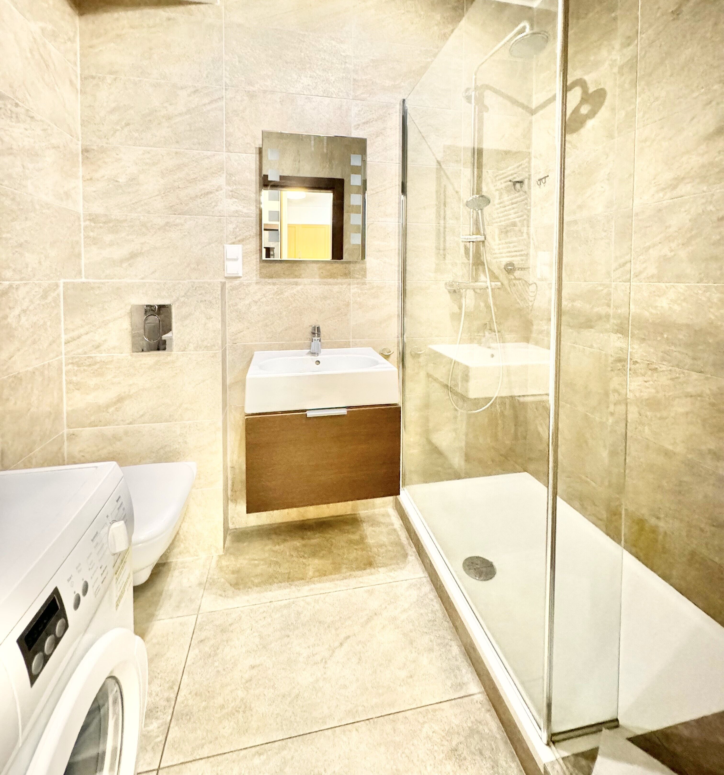 A modern bathroom with a glass shower enclosure, a built-in sink, and a washing machine.