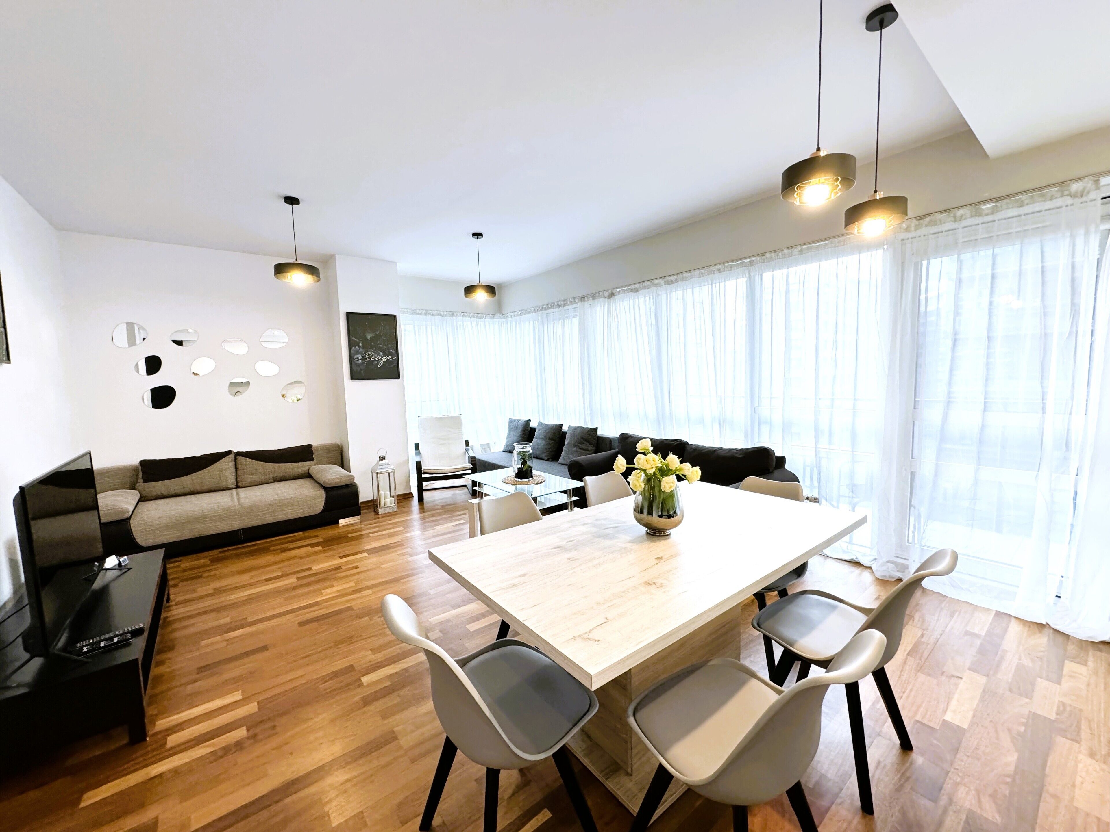 A modern living room with a wooden dining table, two sofas, and a coffee table with flowers.