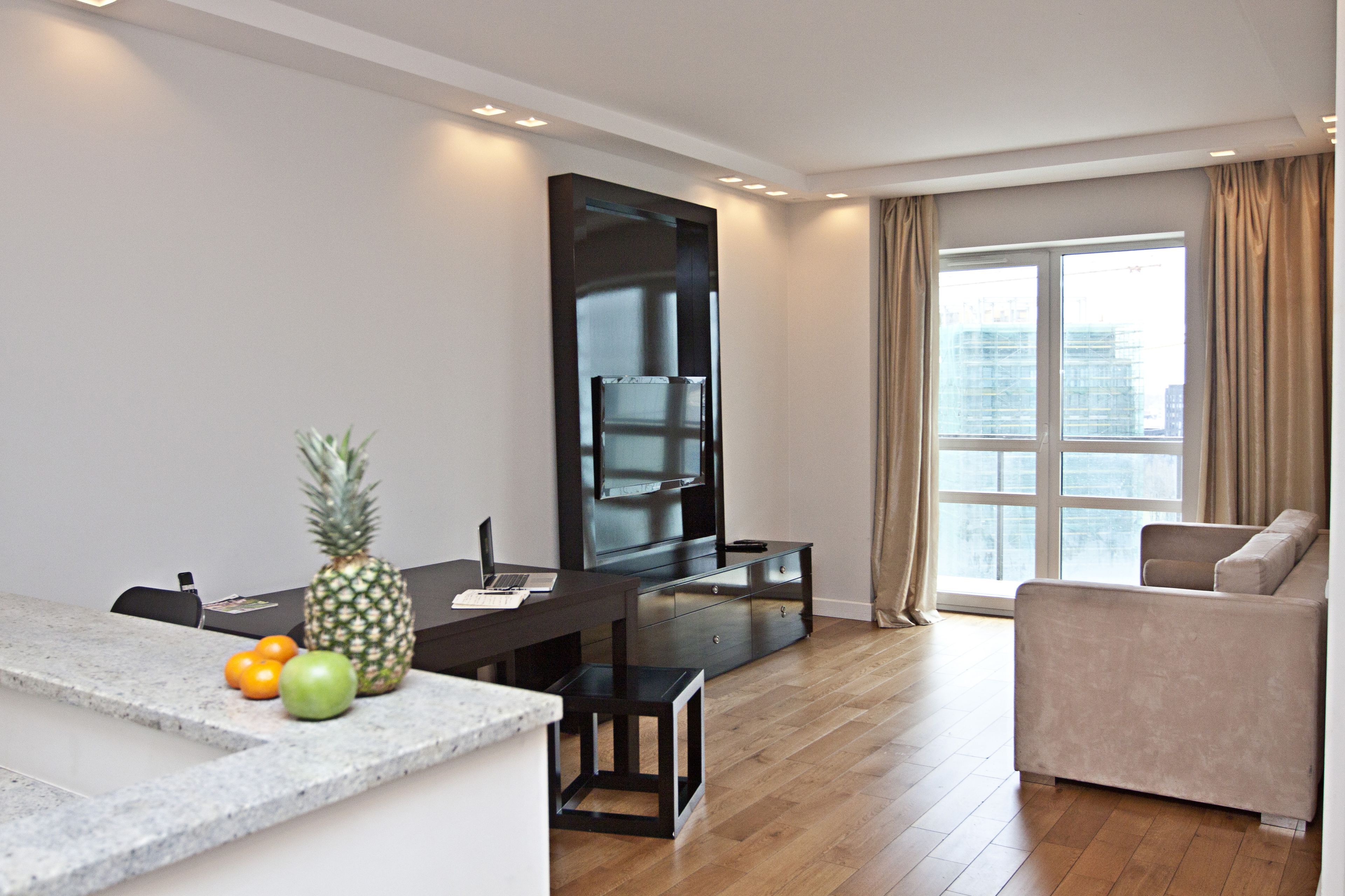 A modern living room with a dining area, a flat-screen TV, a sofa, and a large window with curtains.