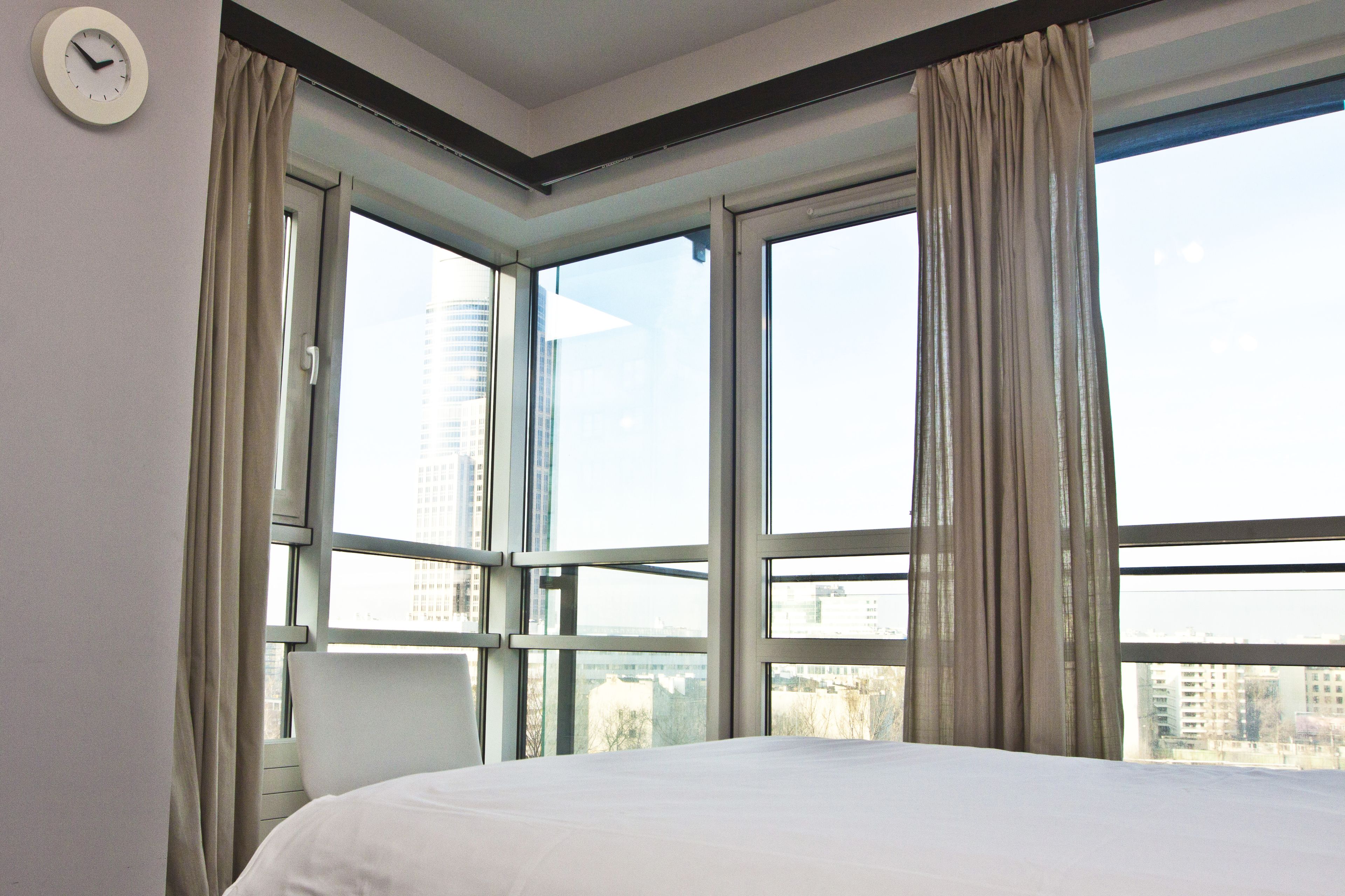 Een hotelkamer met een groot raam, een bed en een wandklok.