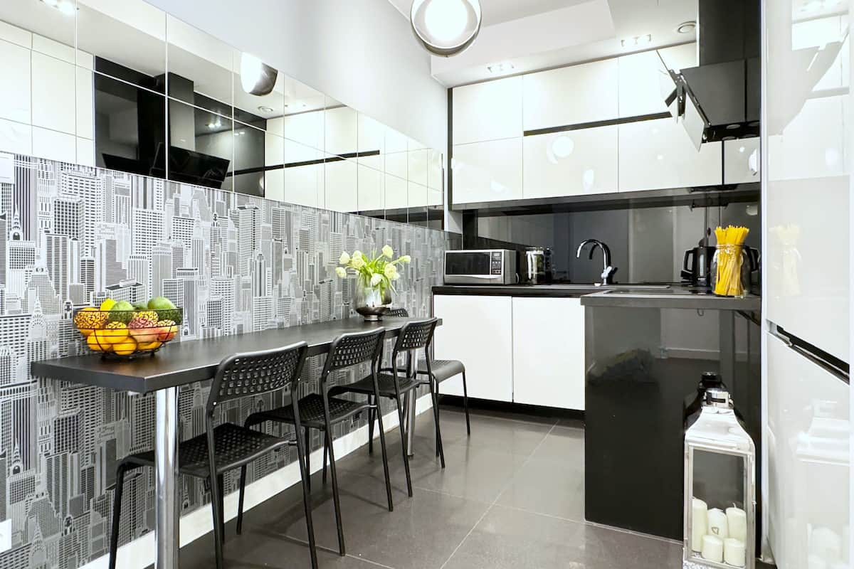 Une cuisine moderne avec des meubles blancs, un plan de travail noir et un revêtement mural représentant un paysage urbain.