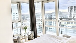 A modern bedroom with a large bed, a glass table with a vase, and a view of the city through large windows. - Platinum Towers Country 2 Country (Warsaw)