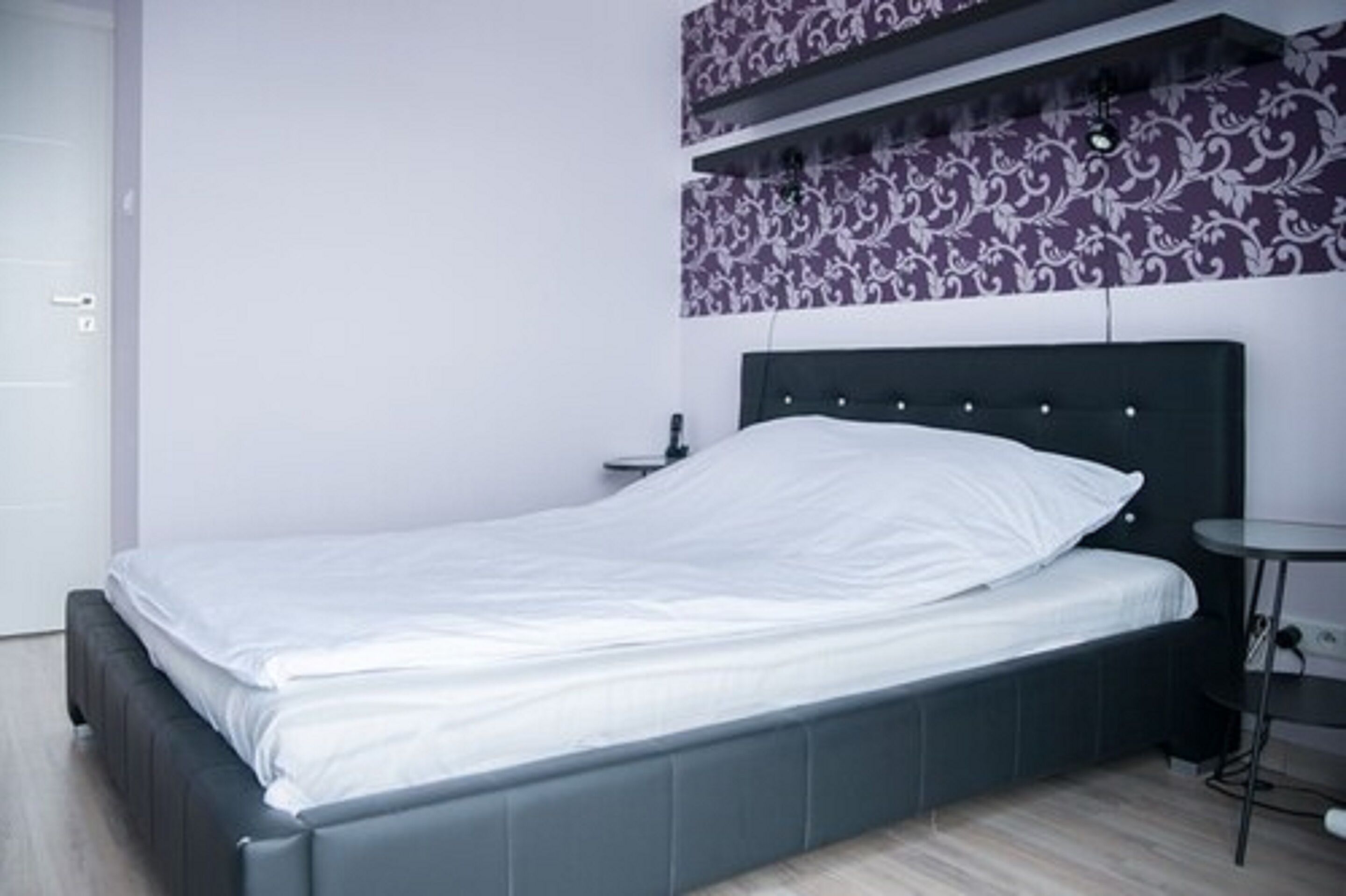 Camera da letto moderna con testiera scura, copripiumino bianco e un comodino.