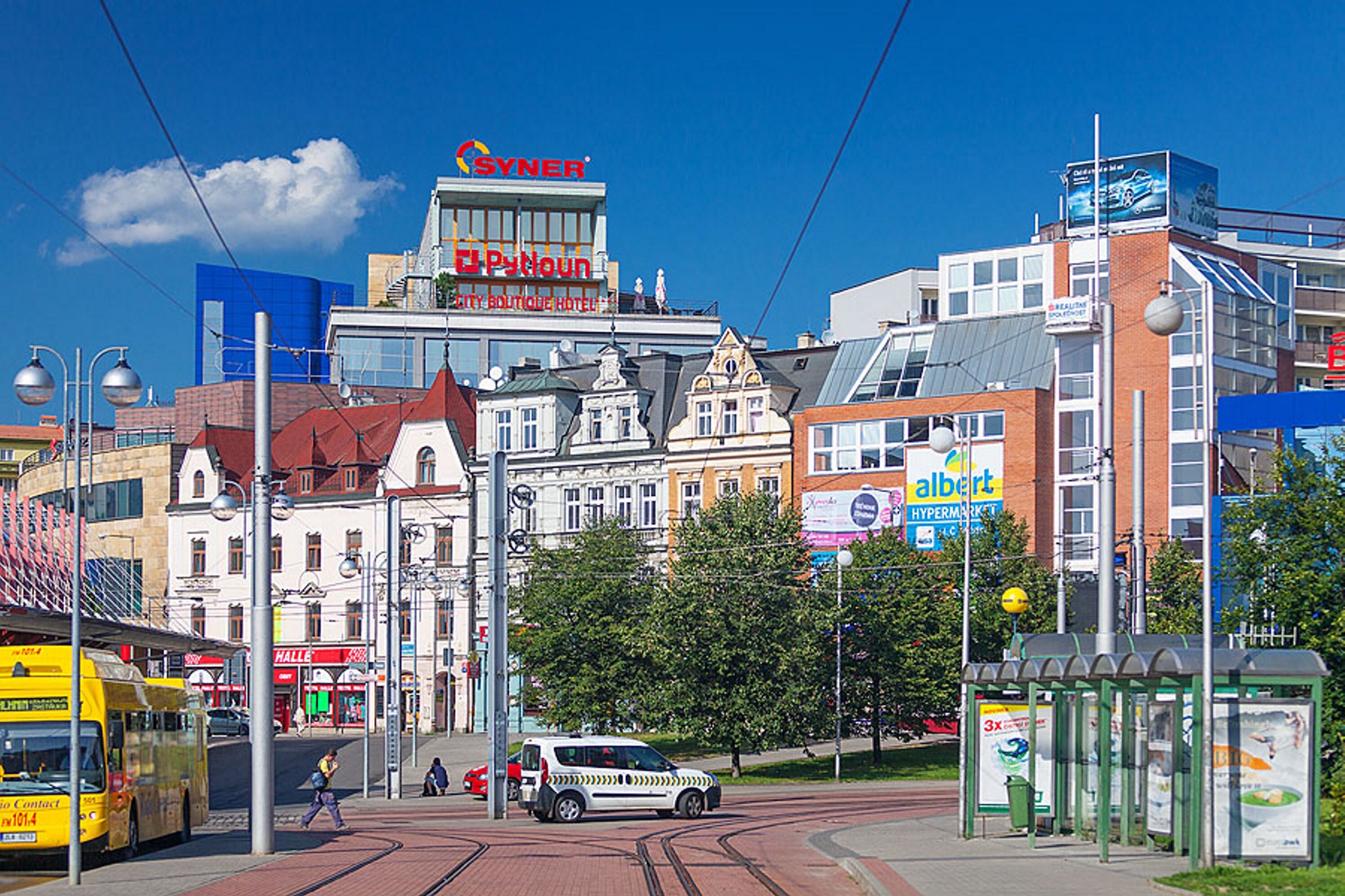 A city street with a mix of modern and historic buildings, a tram, and a bus.