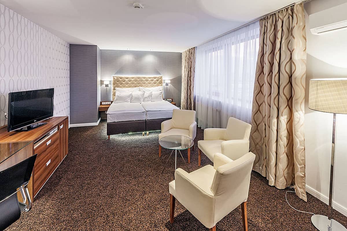 A hotel room with a bed, a TV, a desk, and two chairs.