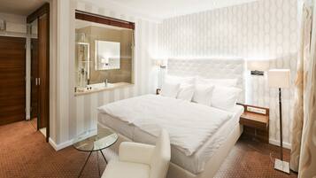 A hotel room with a large bed, a glass table, a chair, a wardrobe, and a mirror.