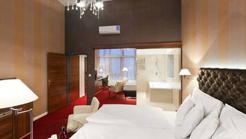 A hotel room with a large bed, a desk, a chair, a small table, a mirror, and a chandelier.