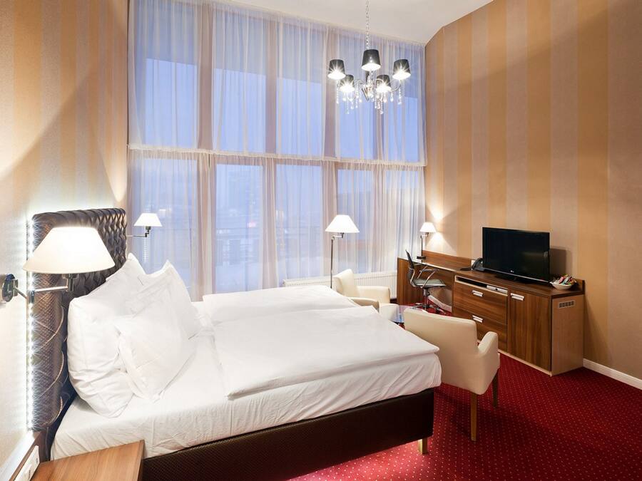 Una habitación de hotel con una cama grande, dos lámparas de noche, un televisor y un aparador de madera.