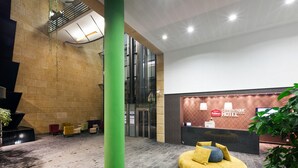 A hotel lobby with a reception desk, a green pillar, and a yellow seating area.