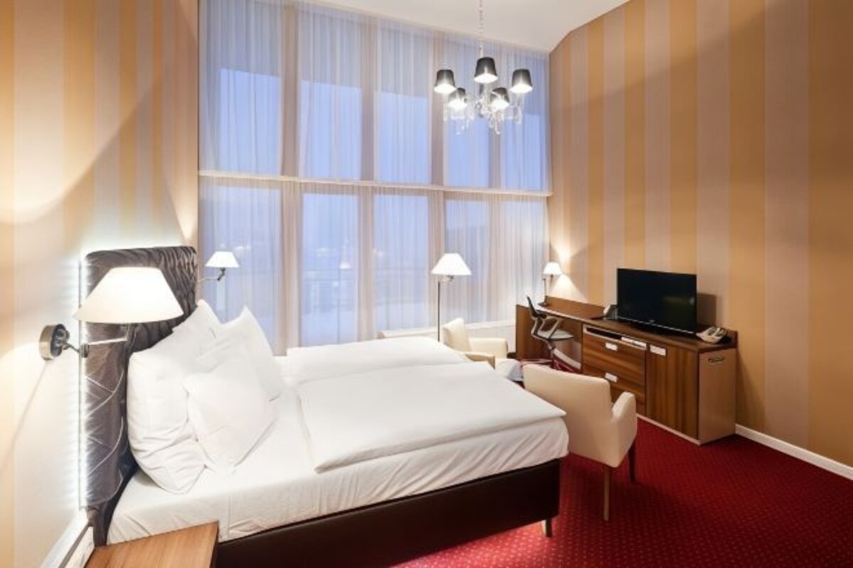 A hotel room with a large bed, a desk with a TV, and a window with curtains.