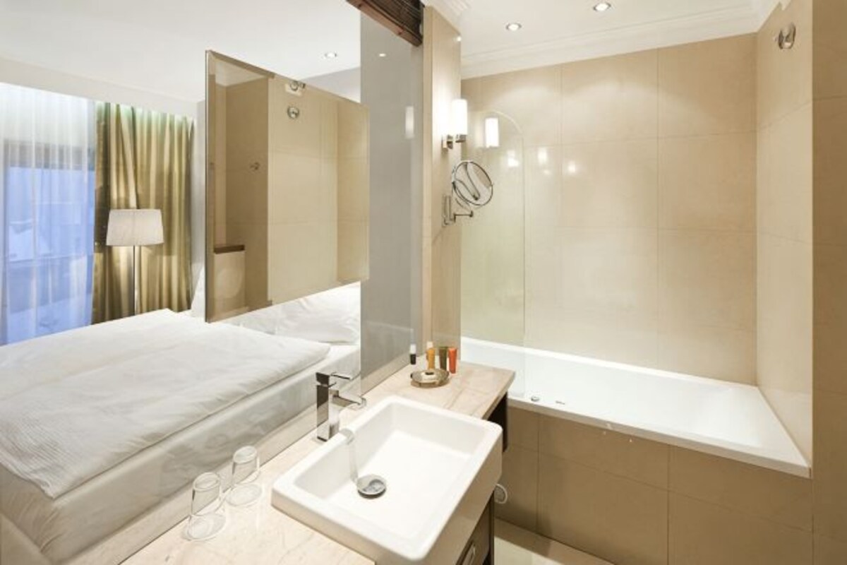 A modern hotel room with a large bed, a bathroom with a bathtub, and a large mirror.
