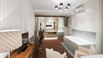 Habitación de hotel moderna con televisión, escritorio, sillas, un ventanal grande y baño con bañera y ducha.