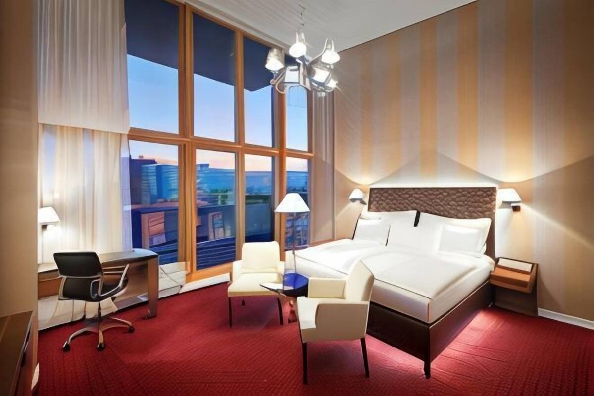 A hotel room with a large bed, a desk, two chairs, a small table, and a view of the city.