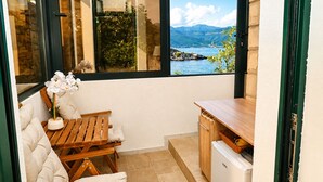 Un balcon avec une table en bois, un banc rembourré, un petit réfrigérateur et une vue sur un lac et des montagnes.