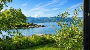 Une vue sur un lac, avec des montagnes en arrière-plan, une zone herbeuse au premier plan et un cadre de fenêtre sur la droite.