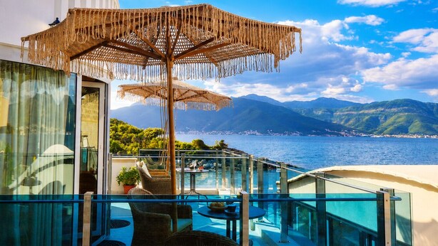 Un balcon doté d’une balustrade en verre, d’un parasol en osier, d’une piscine et offrant une vue sur la mer et les montagnes.