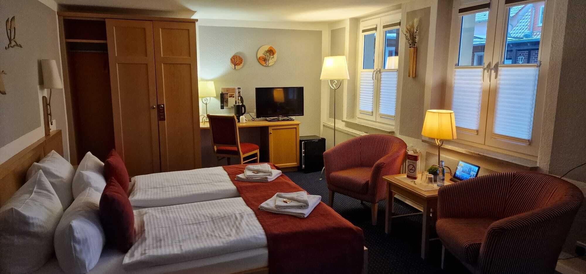 Une chambre d’hôtel avec deux lits, un bureau avec un ordinateur, une télévision et une chaise.
