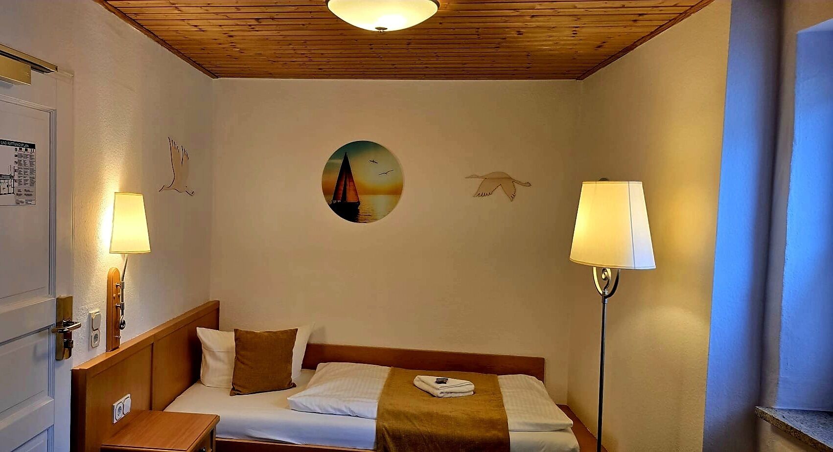 Een hotelkamer met een bed, twee bedlampen, een wandklok en een lijst met een afbeelding.