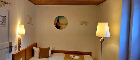 Een hotelkamer met een bed, twee bedlampen, een wandklok en een lijst met een afbeelding.