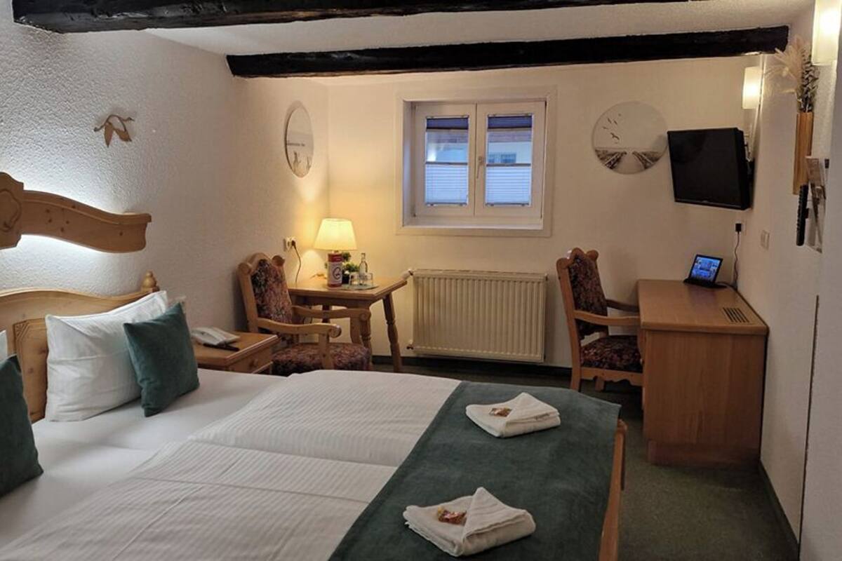 A bedroom with a wooden bed, a desk, a chair, a lamp, a TV, and a window.